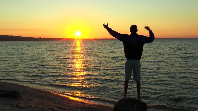Man waving his arms rising sun over the sea