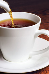 Pouring tea from a pot into an white cup