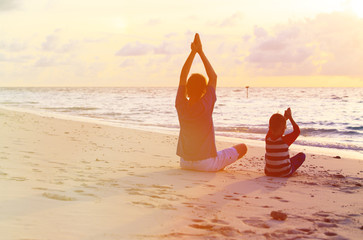 father and son doing yoga at sunset sea