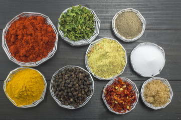 Different spices in shiny bowls on a dark wooden table