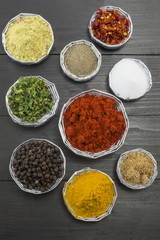 Various spices in shiny bowls on a dark wooden table