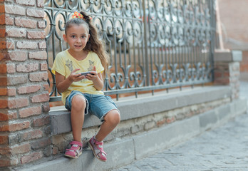 girl is sitting outdoor and playing on the phone