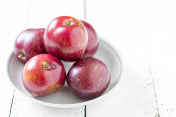big ripe plums/ big ripe plums in a ceramic saucer on white boards closeup