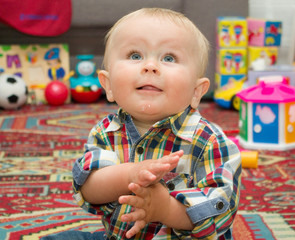 Little blond boy in checkered shirt is sitting on a floor with bright toys background - 88477767