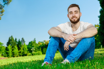 Naklejka na ściany i meble Young man sitting on the grass in park