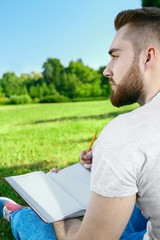 Young man sitting on the grass in park with diary