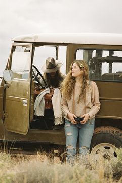 Two women by a jeep in the desert, one holding a camera. 