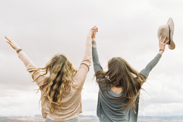 Rear view of two women standing side by side, holding hands, with their arms raised up in the air.