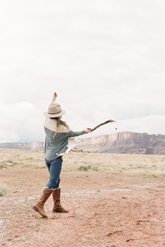 A woman with her arms raised, hitting a stone with a stick into the distance.
