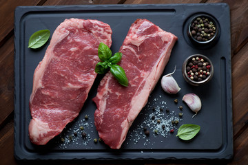Raw striploin steaks with herbs and spices on a basalt plate