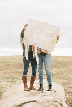 Two women standing holding up a large map in front of their faces.
