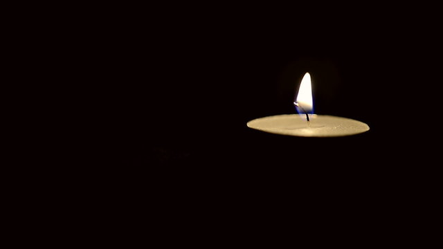 Still candle flame in windless conditions on a black background, shallow depth of field with focus on wick