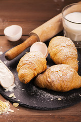 Fresh baked croissants with almond leaves on the wooden table. Selective focus