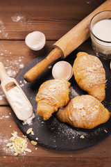 Fresh baked croissants with almond leaves on the wooden table. Selective focus