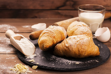 Fresh baked croissants with almond leaves on the wooden table. Selective focus