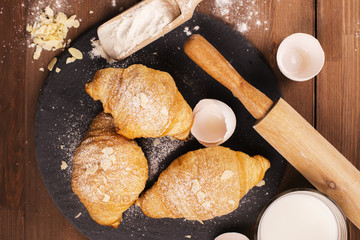 Fresh baked croissants with almond leaves on the wooden table. Selective focus