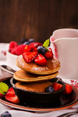 Stack of pancakes with fresh strawberry, honey and mint in frying pan on wooden rustic background. Selective focus