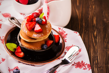 Stack of pancakes with fresh strawberry, honey and mint in frying pan on wooden rustic background. Selective focus
