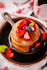 Stack of pancakes with fresh strawberry, honey and mint in frying pan on wooden rustic background. Selective focus