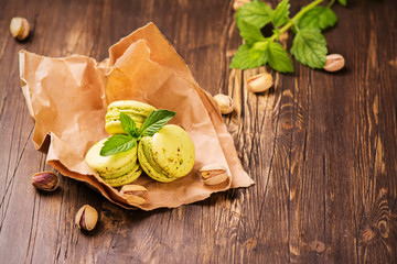 Green pistachio macaroons with nuts and mint on dark rustic wooden background. Selective focus. Toned image