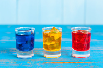 Blue, yellow, rad berry drink or liqueur with ice cube on light