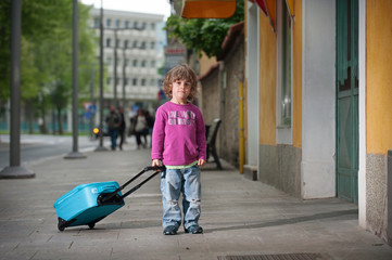 Little boy with a luggage trolley standing on the street. Independence, growing up concept.