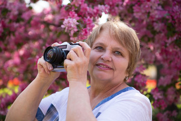 Portrait of woman with camera under pink flowers in summer 