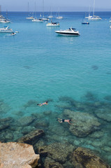 Two people are snorkeling near the rocks and boats