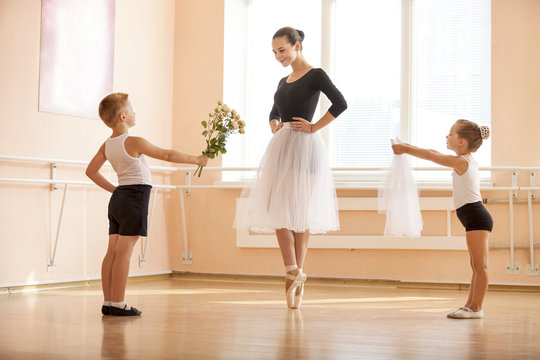 At ballet dancing class: young boy and girl giving flowers and veil to older student while she is dancing en pointe 