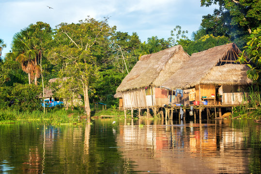 Late afternoon view of a shack on stilts in the Amazon rain forest with a beautiful reflection in the river