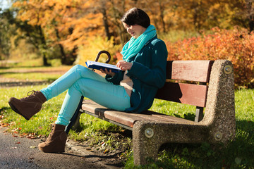 Girl relaxing in autumnal park reading book. Fall.