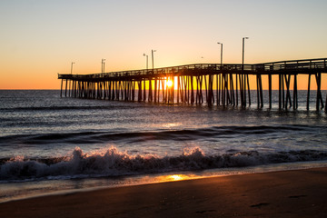 Sunrise with the Virginia Beach fishing pier in silhouette with waves crashing in foreground