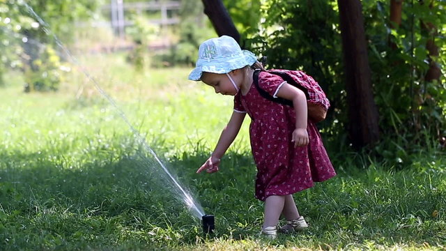 Little girl dabbles with Sprinkle sunny summer day in the park. The concept of a happy childhood.