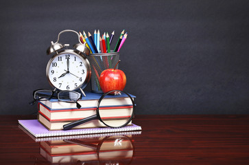 Books, apple, alarm clock and pencils on wood desk table and bla