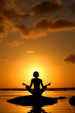 Silhouette of woman practicing yoga during sunset at the seaside