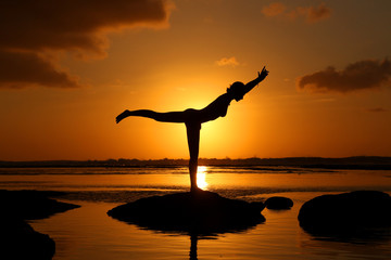 Silhouette of woman practicing yoga during sunset at the seaside