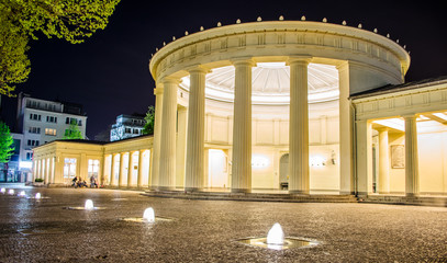 People are sitting in front of illuminated elisenbrunnen in german Aachen.