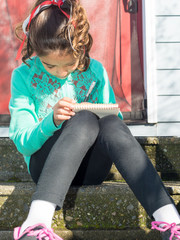 Young Girl Sitting Down Writing In Notepad