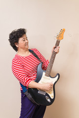 Portrait of adult asian woman with electric guitar on reddish ye