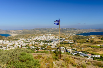 The Greek flag in a picturesque place - Plaka village, views of the coast, Milos island, Cyclades, Greece.