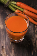 Glass of fresh-squeezed carrot juice and organic carrot on old rustic wooden table. Vintage style....