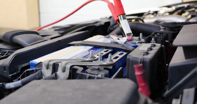 My car battery is dead / Low angle shot of a person connecting the booster cables to the car battery
