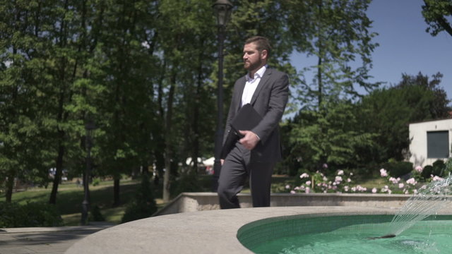 Businessman sits on wall next to the fountain.
