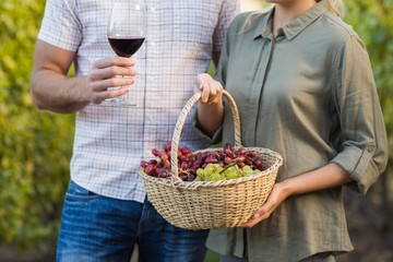 Two vintners holding a basket of grapes and red wine glass 