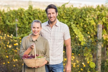 Two young happy vintners holding a basket of grapes