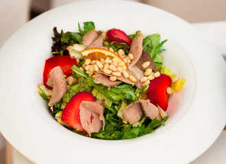 Meat salad with arugula and strawberries on a white plate