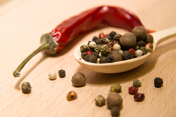 Spoon filled with a mixture of grains of pepper are on a wooden