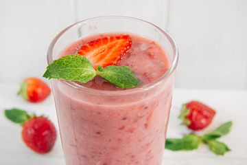 A glass of strawberry smoothie on white wooden table