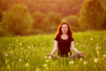 Young woman in the lotus pose on a evening meadow