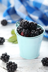 Beautiful ripe blackberry in bucket on white wooden background